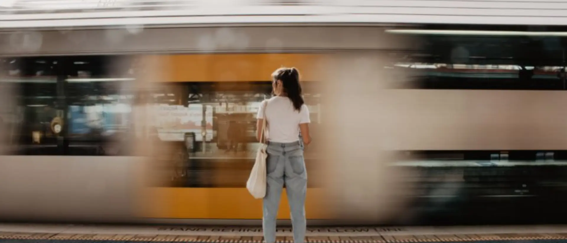 Una mujer de espaldas en una estación de tren moderna, mirando hacia las vías que se pierden en el horizonte. Imagen metafórica sobre vivir el presente y la gestión emocional del tiempo de MRC Training.