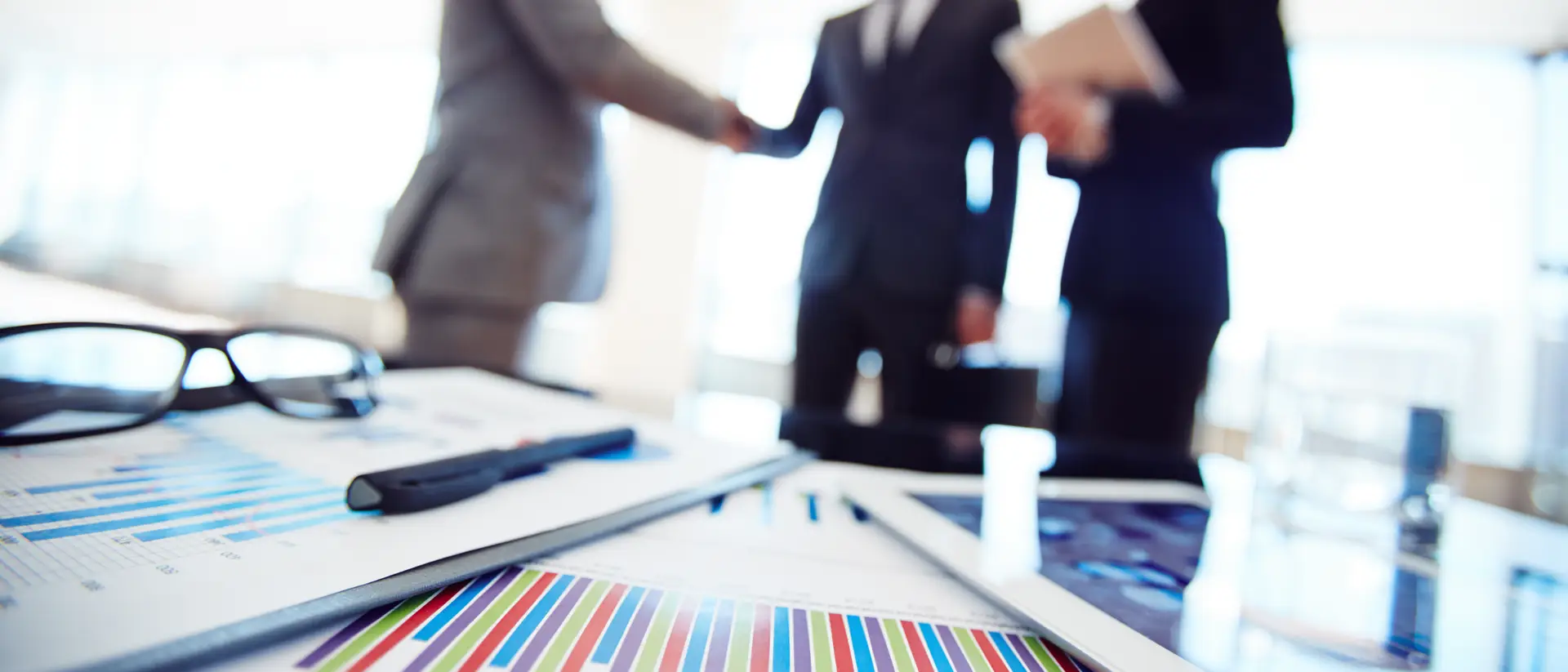 Gráficos de resultados comerciales sobre un escritorio con tres profesionales cerrando un acuerdo basado en la confianza de fondo. Concepto de vender sin vender | MRC