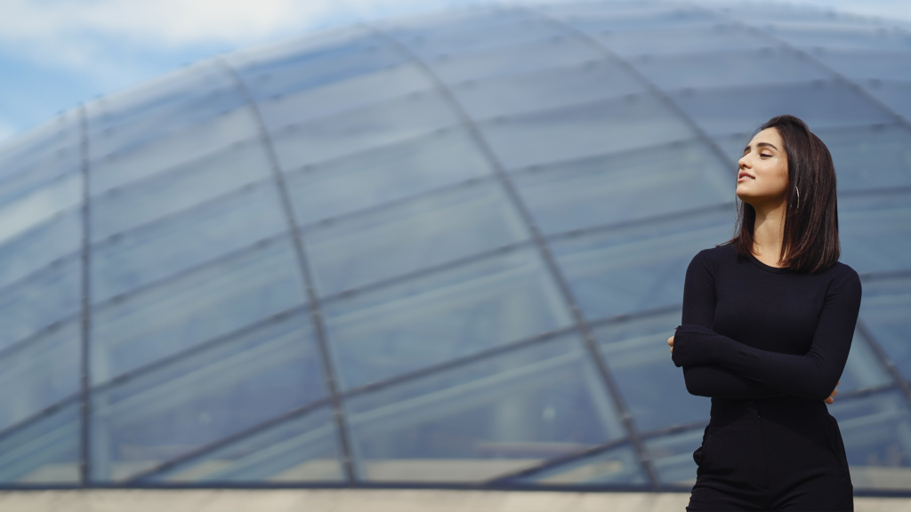 Directiva con los brazos cruzados y mirada serena frente a una estructura arquitectónica, representando el liderazgo consciente