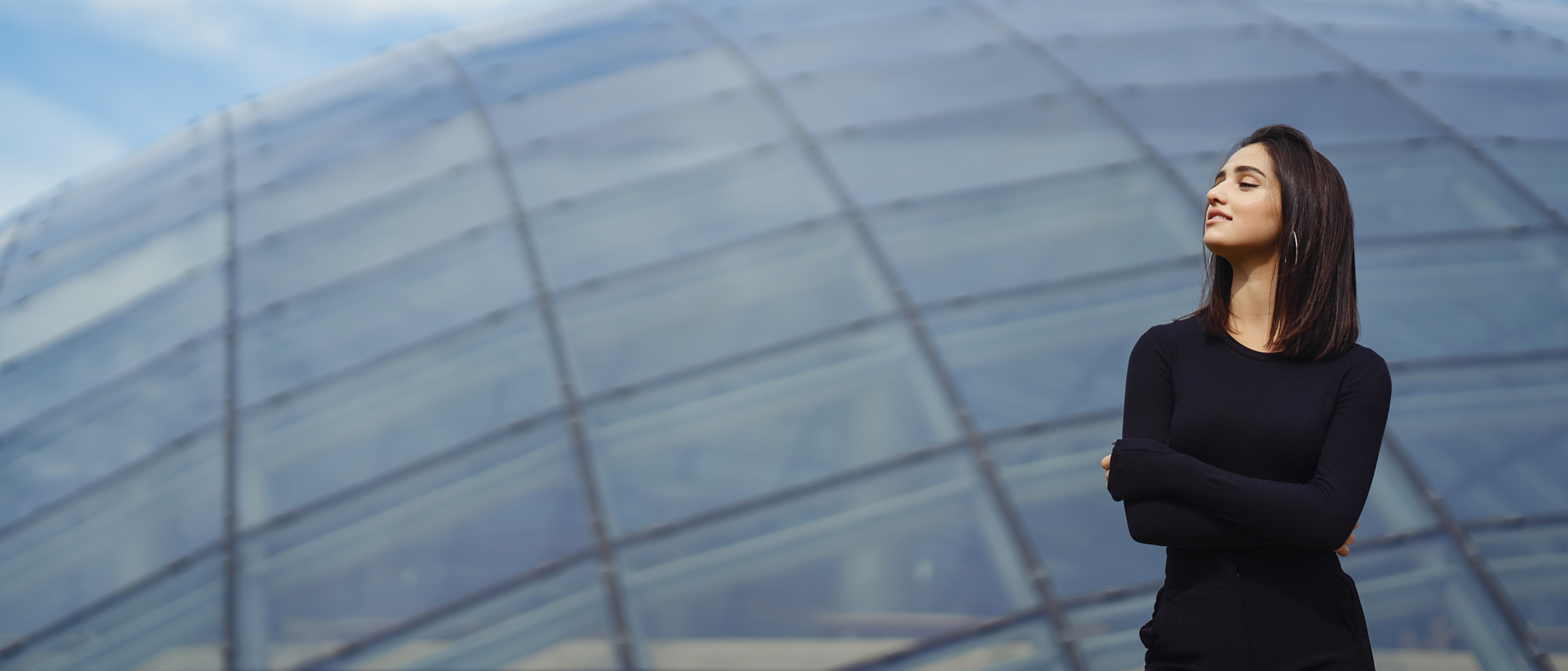 Directiva con los brazos cruzados y mirada serena frente a una estructura arquitectónica, representando el liderazgo consciente